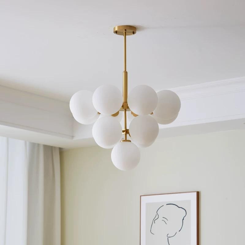 Candelabru cu globuri albe mate pe bara aurie, montat in sufragerie luminoasa cu tavan inalt